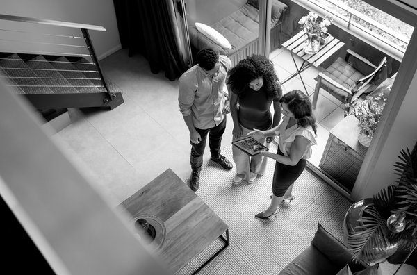 Zwei Frauen und ein Mann stehen in einer Immobilie. Eine der Frauen erklärt etwas.