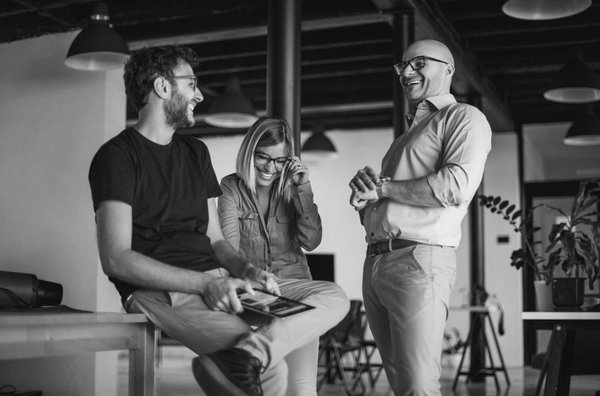 Zwei Männer und eine Frau in lockerer Atmosphäre beim Gespräch in einem modernen Büro, alle lachen herzlich.