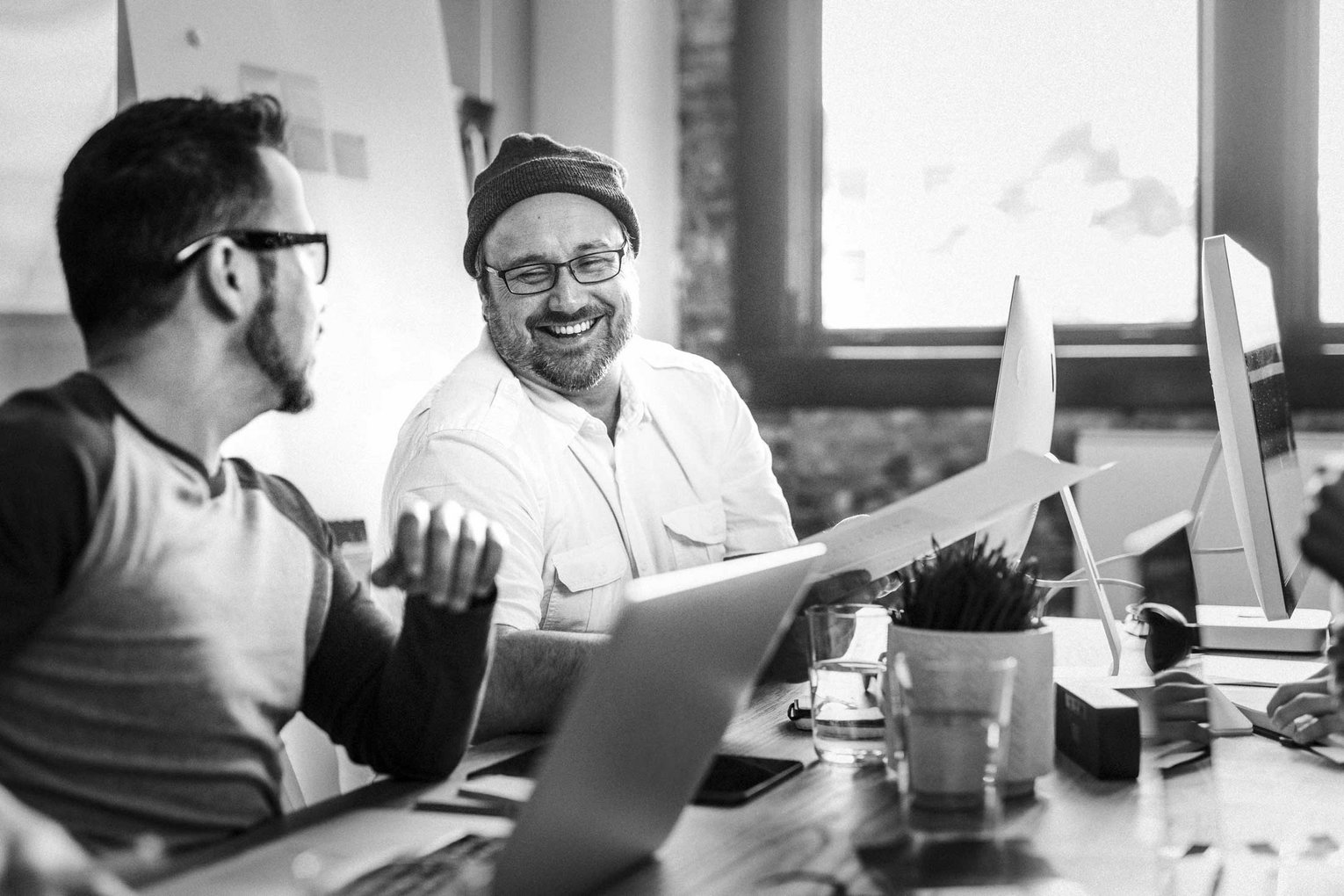 Kollegen im Gespräch im modernen Büro Zwei Männer am Arbeitsplatz in lockerer Unterhaltung, moderne Büroumgebung mit Computern und Tageslicht.